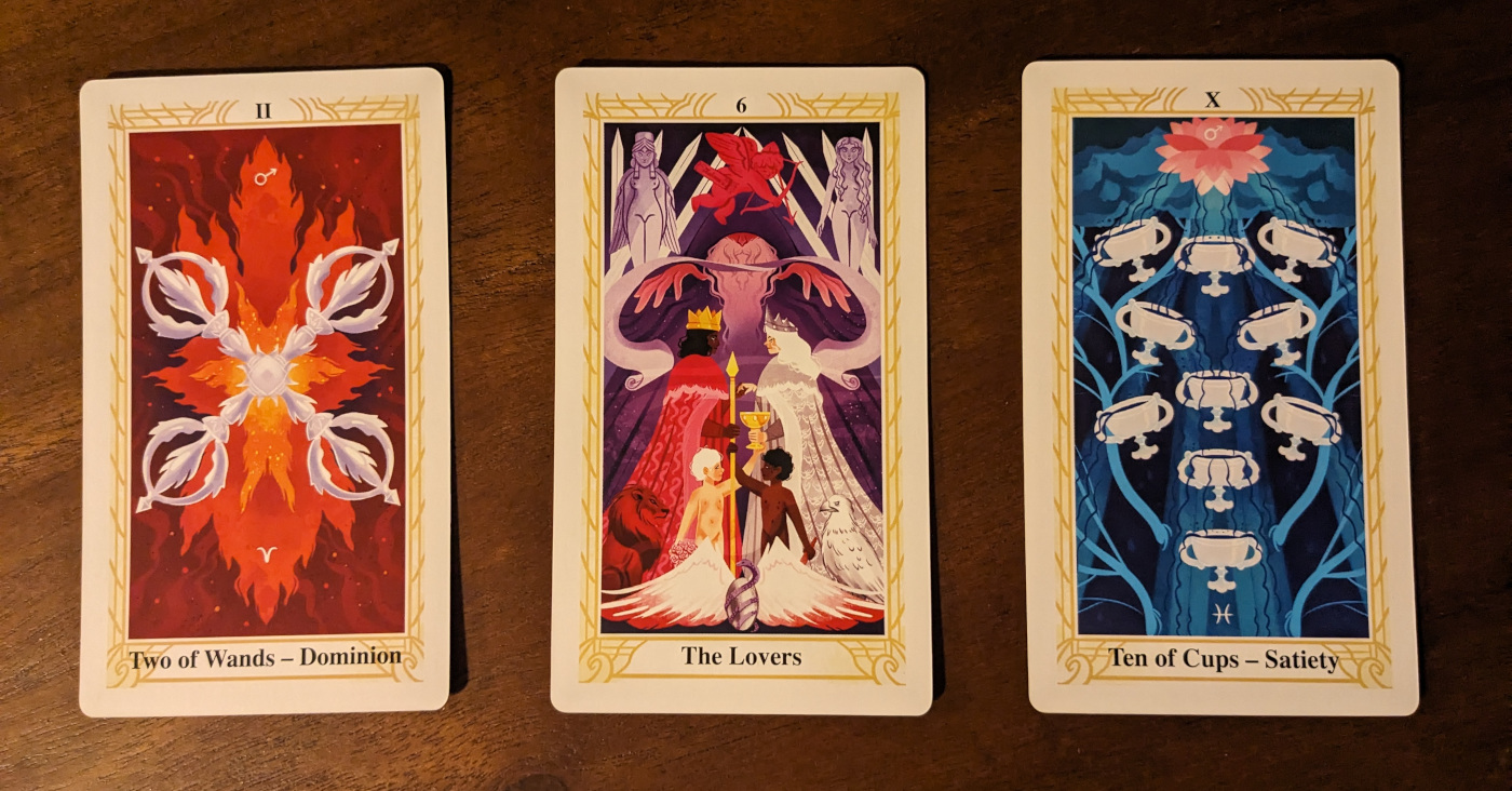 Three tarot cards lined up on a wooden table: The Two of Wands, The Lovers, The Ten of Cups